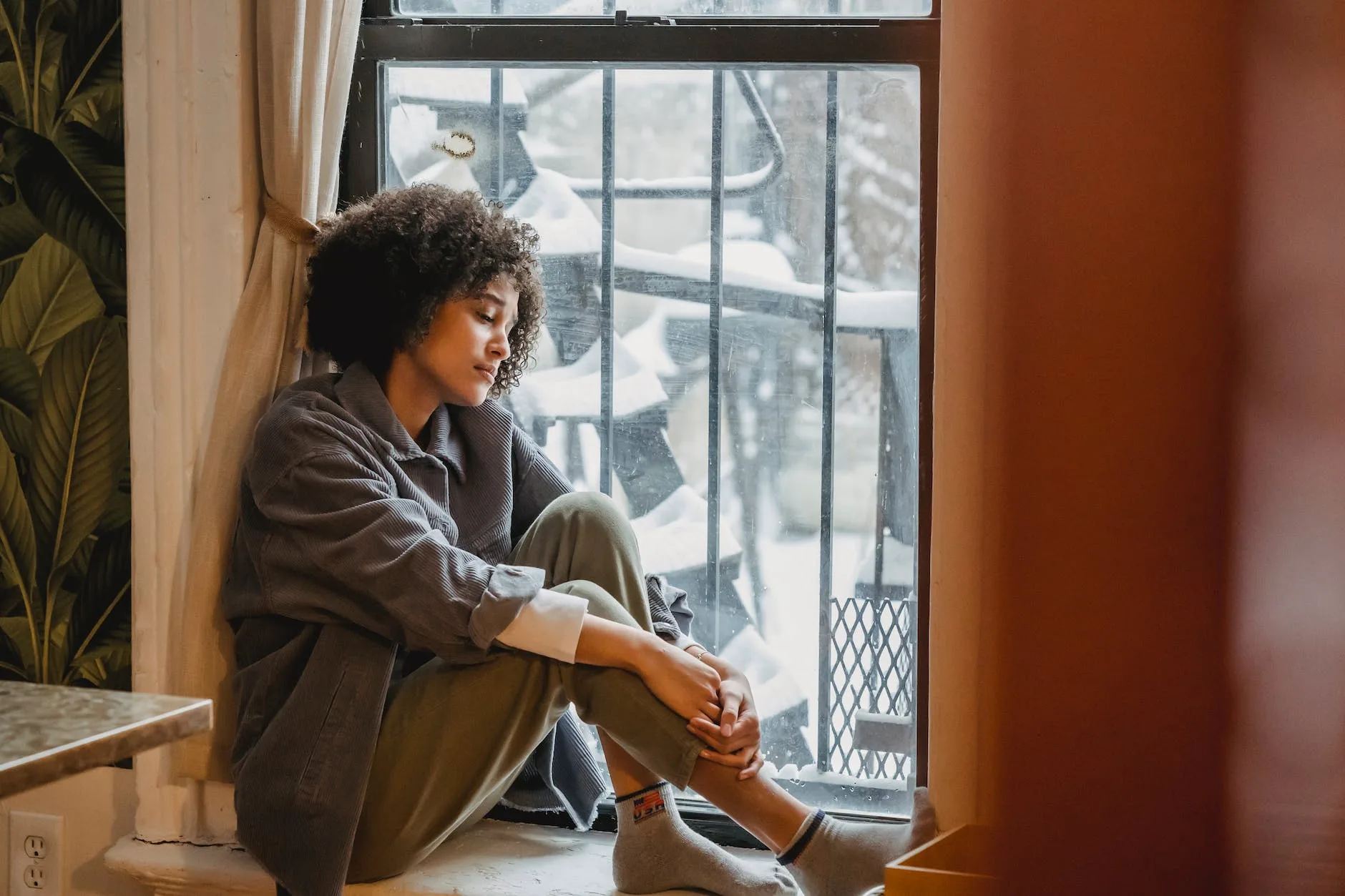 melancholic black female sitting on windowsill